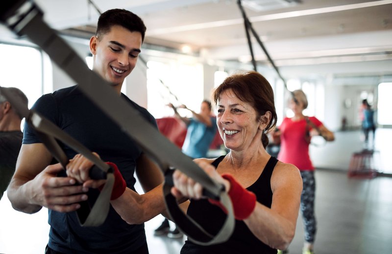 aeltere-frau-trainer-trx-lachen